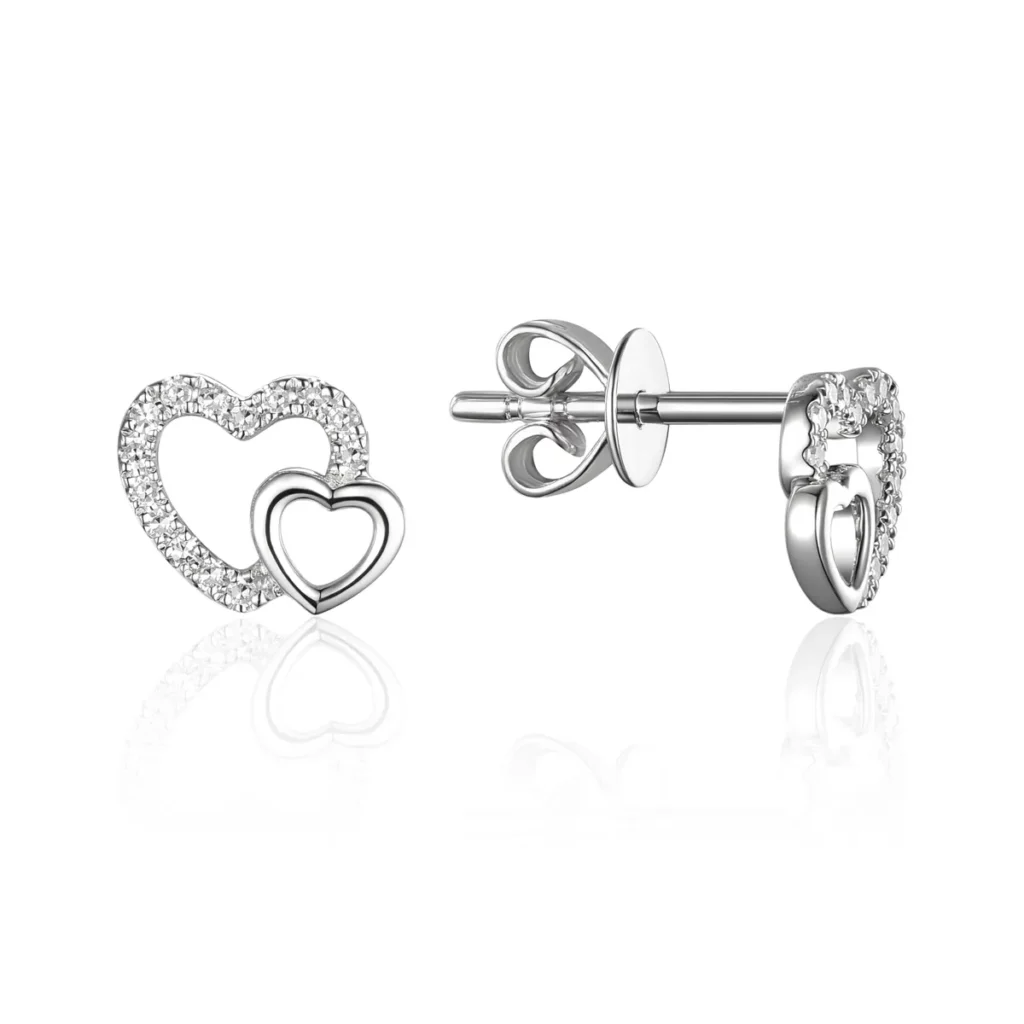 One pair of 14 karat white gold diamond heart stud earrings by Luvente. Each earring contains two open-style hearts with the smaller one set into the bottom of the larger one. The smaller one has a polished finish and the larger one is set with round diamonds. The pair has a total of 28 round single-cut diamonds weighing 0.09 carat total weight with G color and Si2 clarity in pave settings. The front of each earrings is approximately 7mm wide. Friction posts and backs.