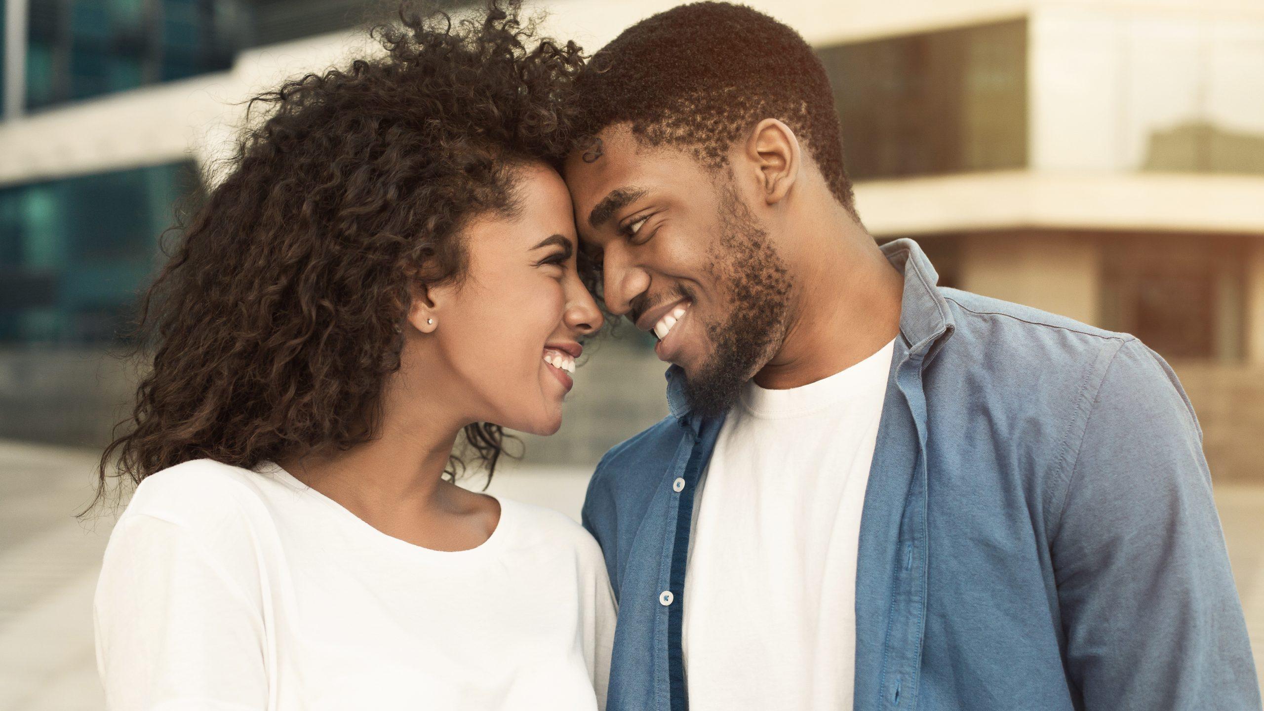 A young attractive couple smiles and tenderly leans their foreheads against each other in a loving and content pose