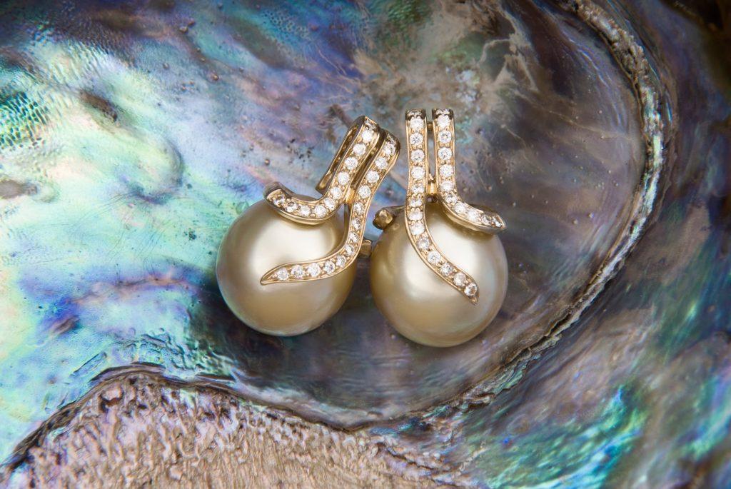 Gold South Sea pearl and diamond earrings laying on an abalone shell